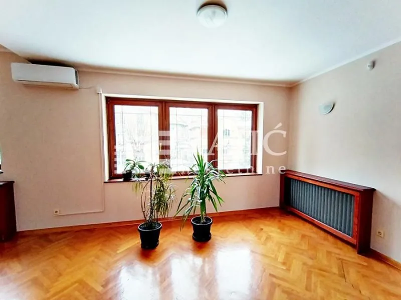 Empty living room with parquet flooring and a large window.