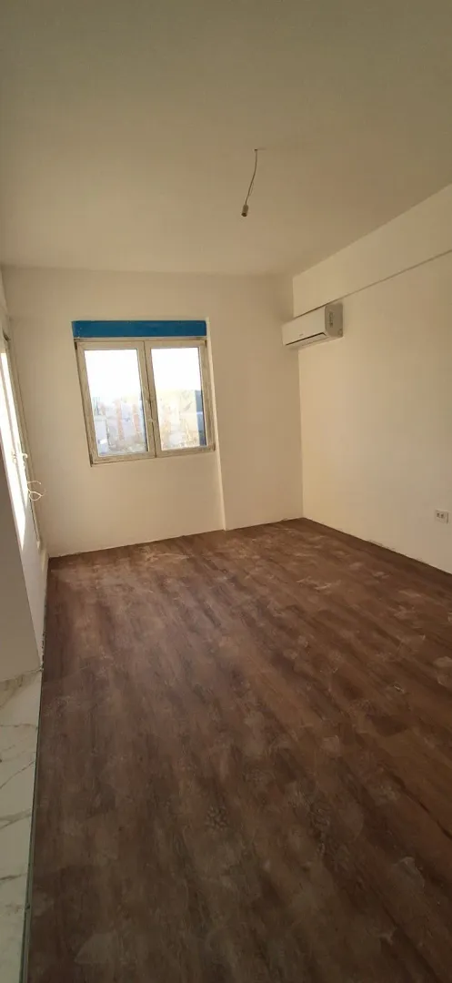 Prazna prostorija sa laminatnim podom i klima uređajem na zidu.