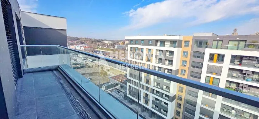 Moderan balkon sa staklenom ogradom i pogledom na okolne zgrade.