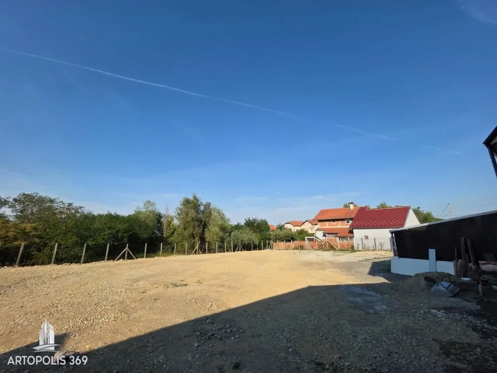 Pogled na ograđeni plac i okolne kuće sa vedrim nebom.