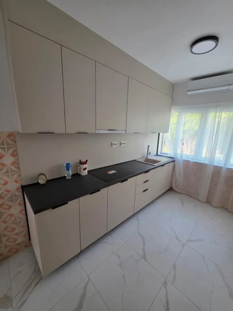 Moderna kuhinja sa bež elementima i tamnom radnom pločom.