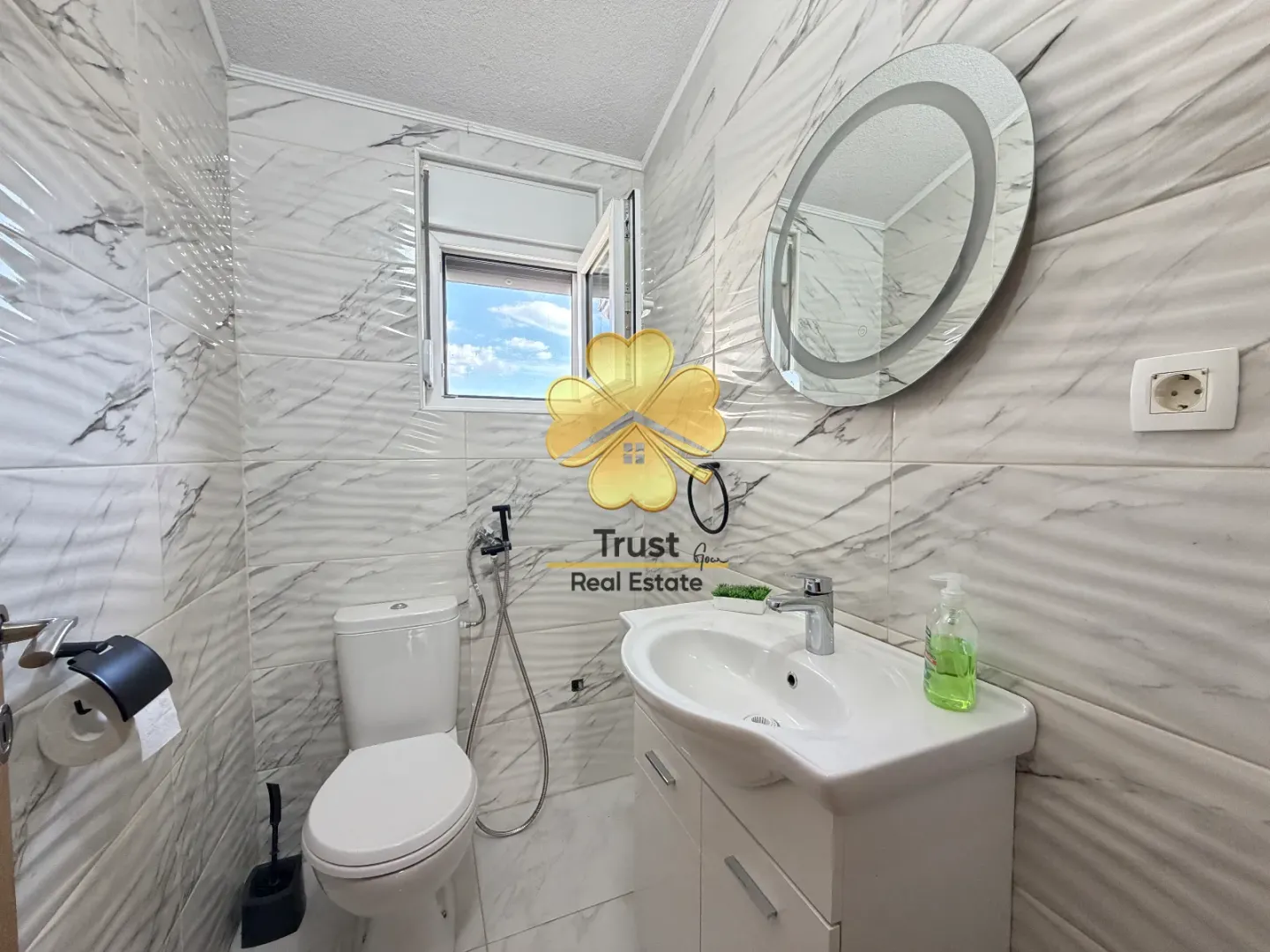 Smaller bathroom tiled with marble-pattern tiles, featuring a sink and toilet.