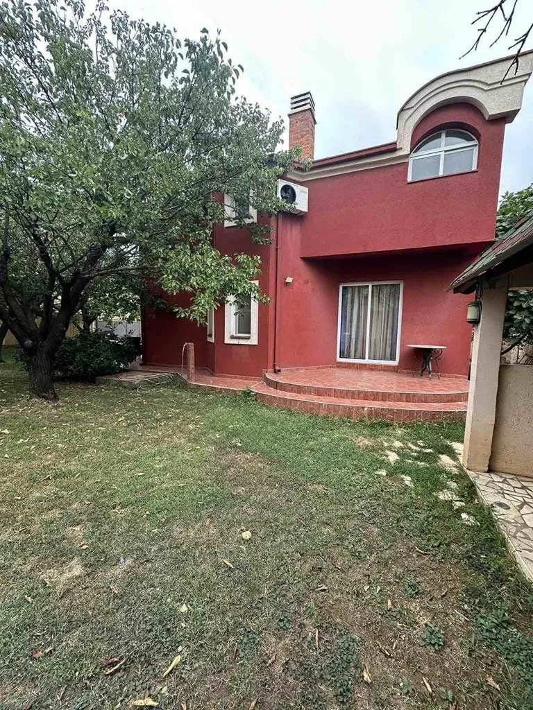 View of the yard and the rear facade of the house with a terrace and greenery.