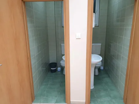 Two toilets with green tiles and wooden doors. - image 12