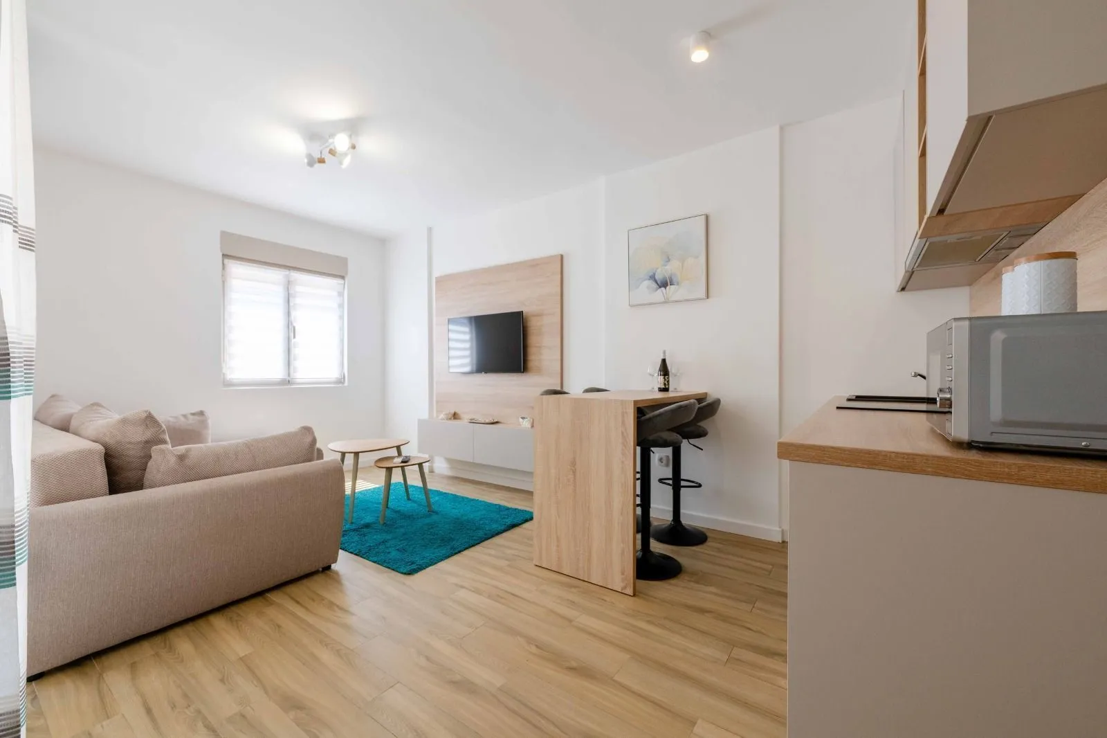Living room with sofa, TV panel, and a dining bar connected to the kitchen.