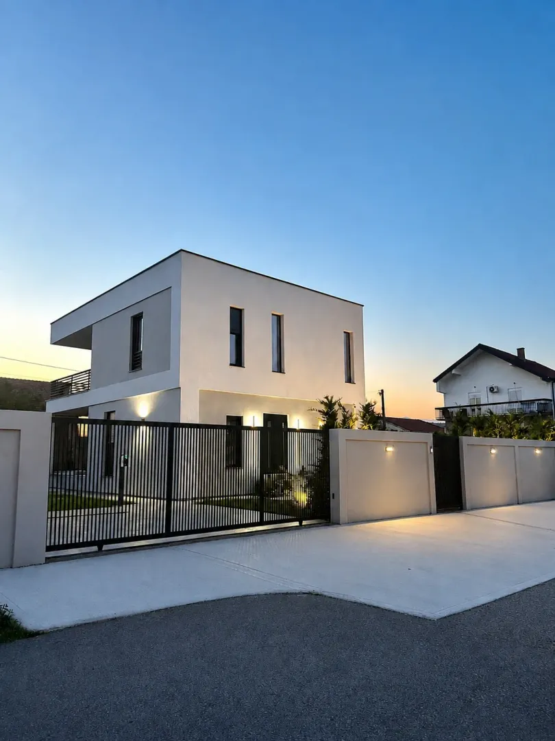 Exterior view of a modern house with illuminated fencing and courtyard at dusk.
