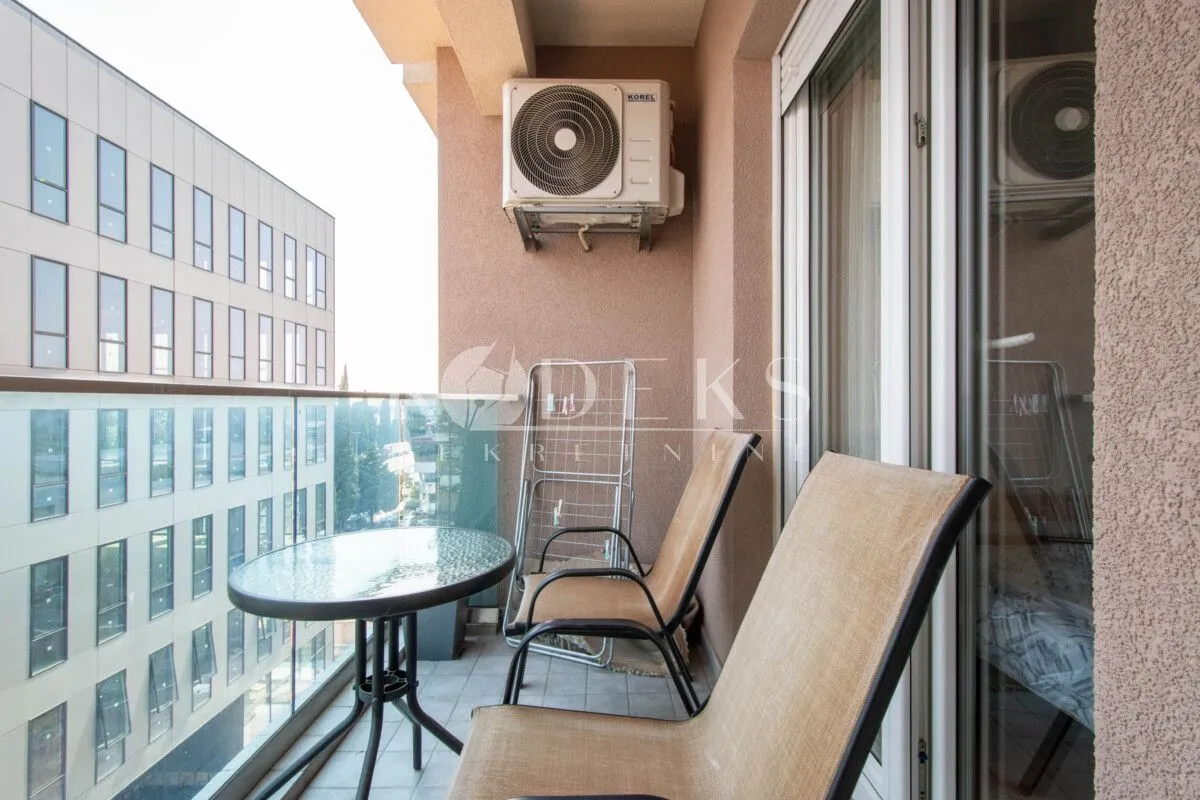 Manji namješteni balkon sa stolom, stolicama i klima uređajem.