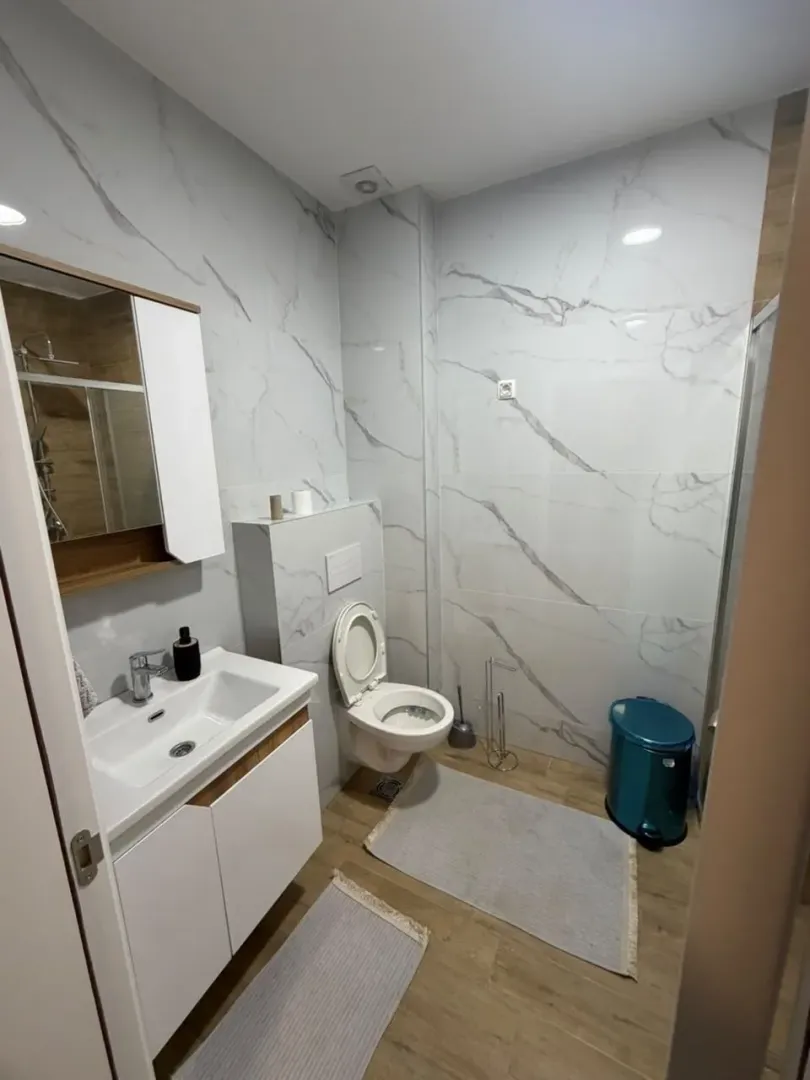 Savremeno opremljeno kupatilo sa bijelim pločicama i sanitarijama.