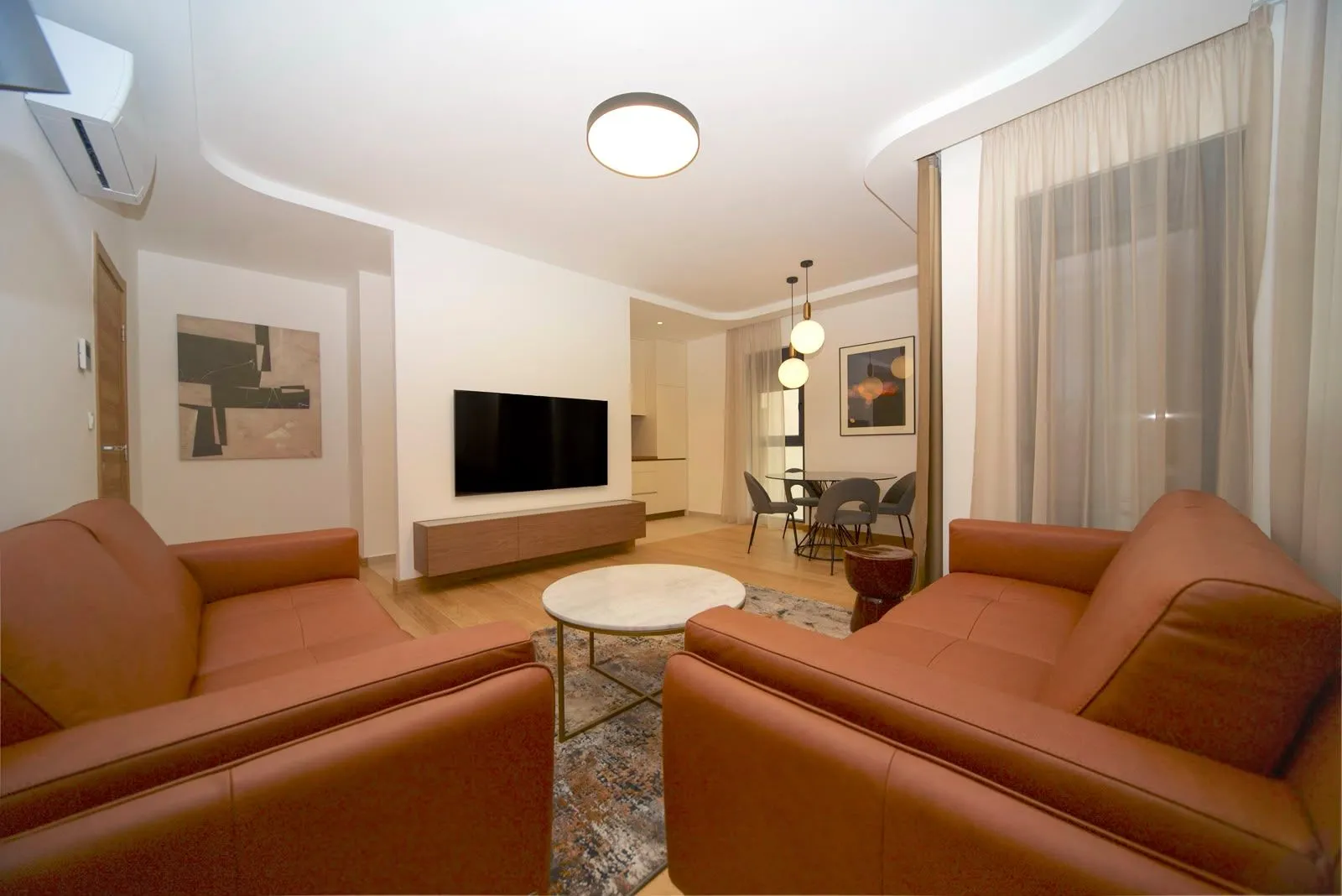 Spacious living room with a sofa set, TV, and dining area in the background.