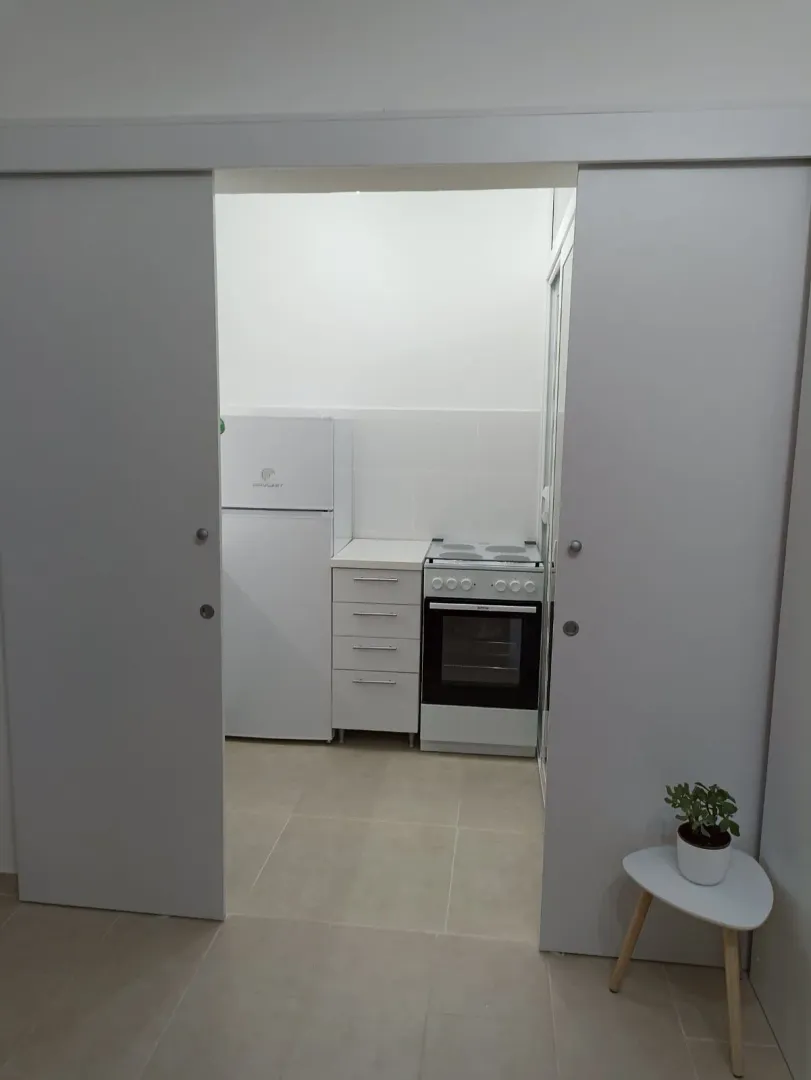 Manja kuhinja sa frižiderom, šporetom i elementima, odvojena kliznim vratima.