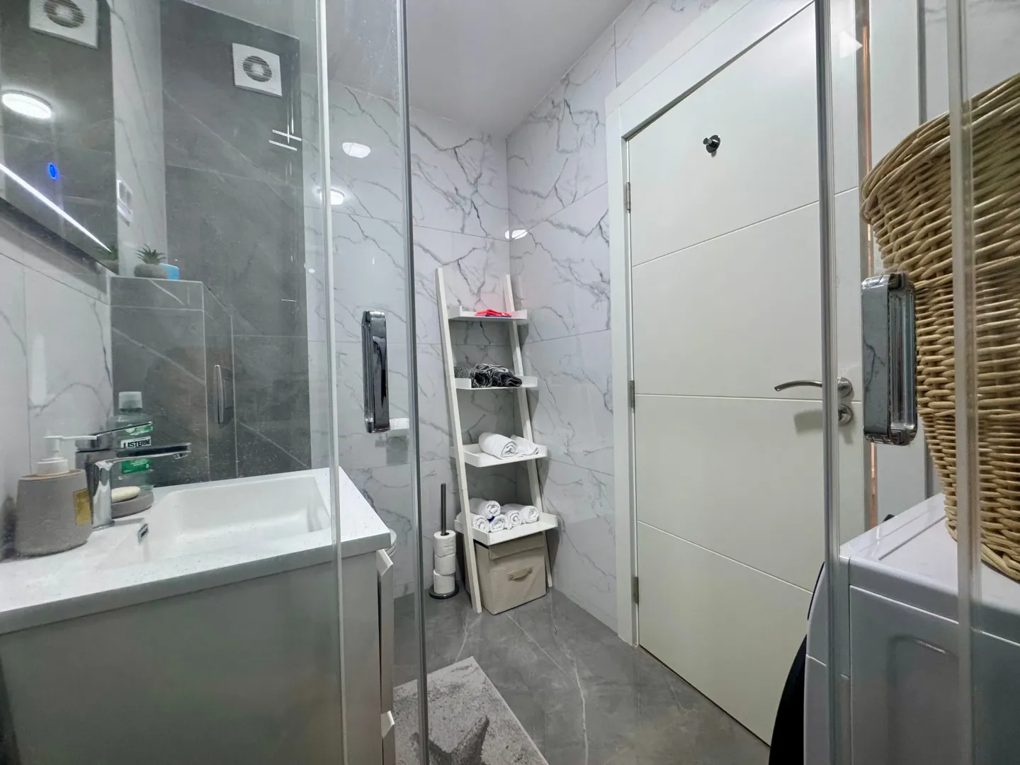Modernly equipped bathroom with a walk-in shower, washbasin, and white marble-effect tiles.