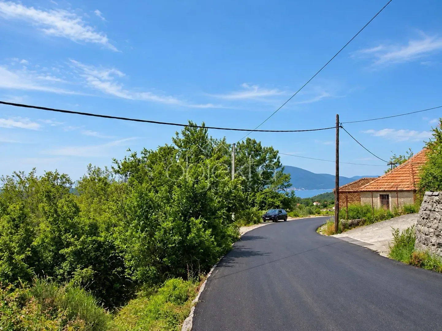 Asfaltirani put koji vodi kroz zeleno okruženje sa pogledom na more.