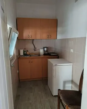 Small kitchen with wooden cabinets, sink, and a small refrigerator. - image 17
