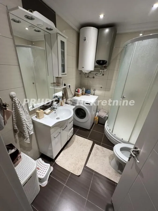 Compact bathroom with a shower cabin, washbasin, toilet, and washing machine.