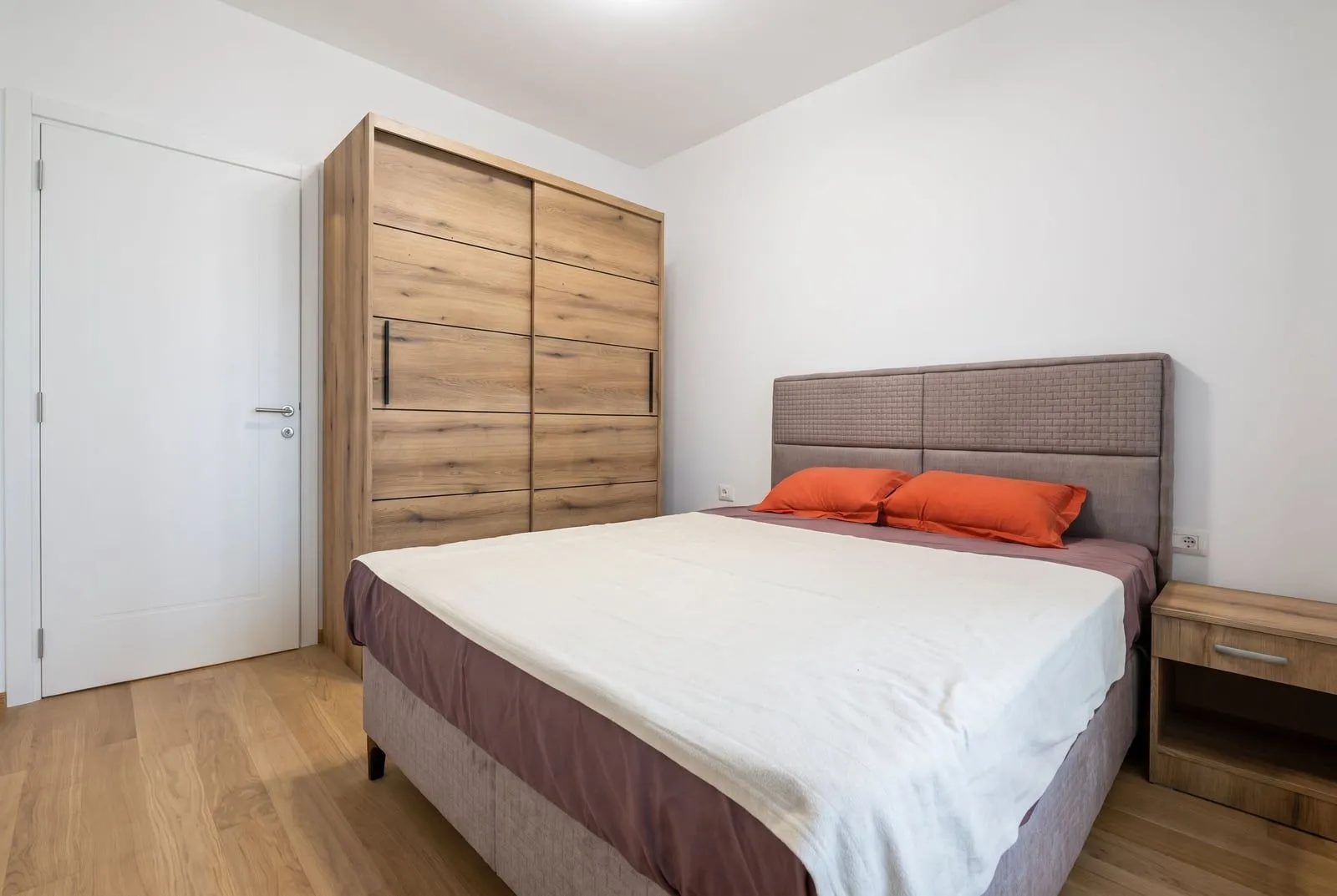 Furnished bedroom with a double bed, large wooden wardrobe, and nightstand.