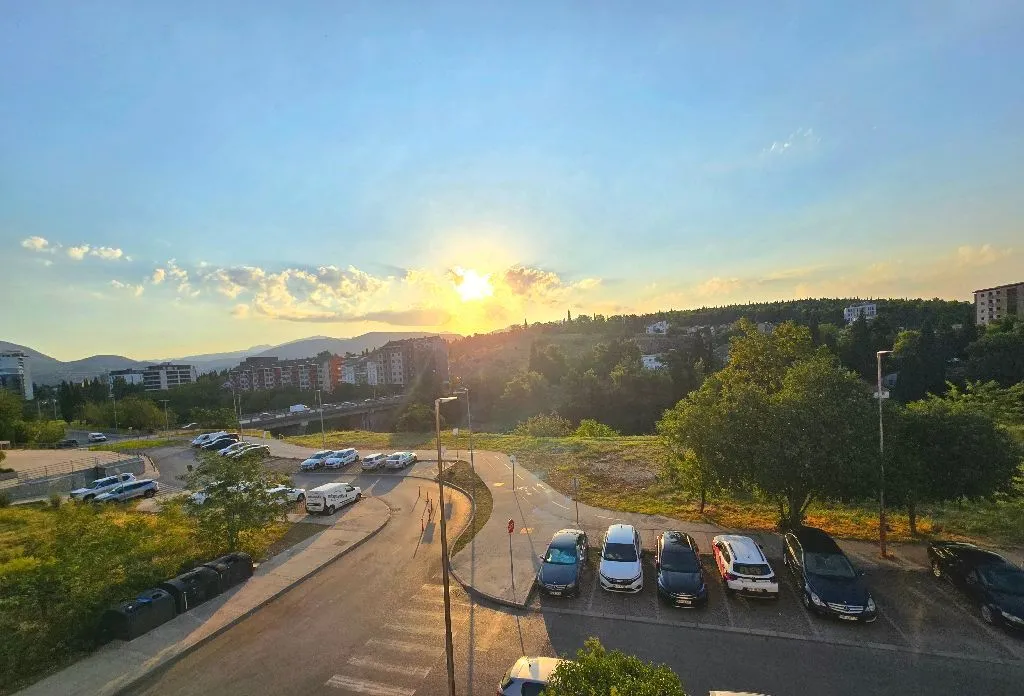 Pogled iz objekta na parking i okolni pejzaž u sumrak.