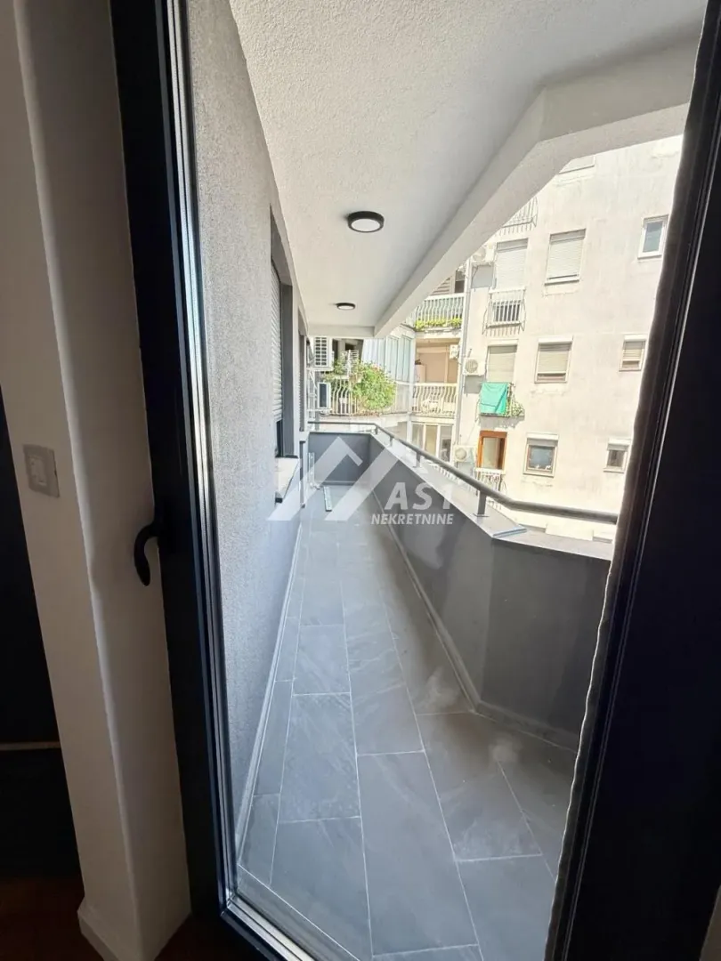 Dugačak popločani balkon sa pogledom na susedne zgrade.