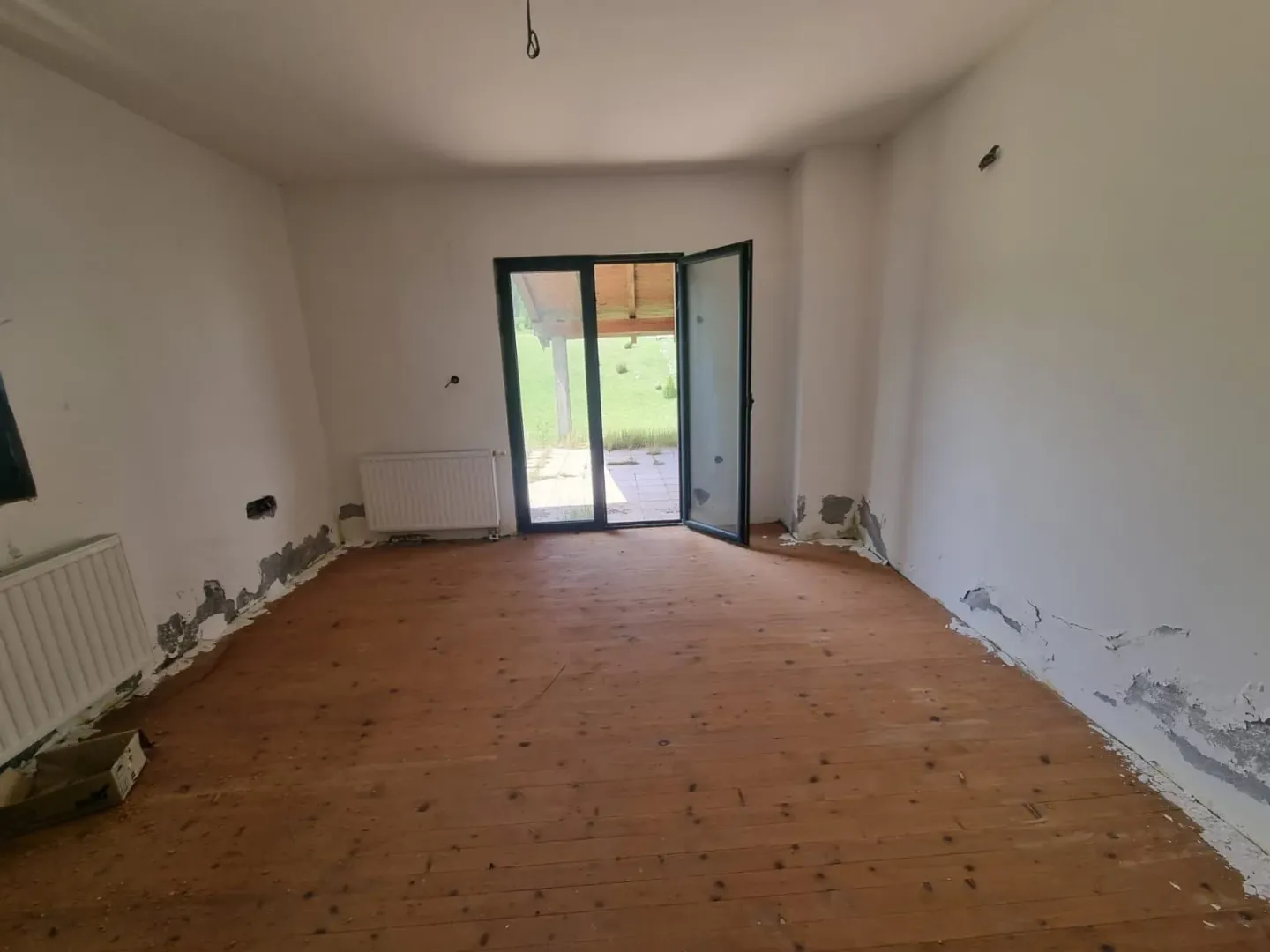 Prazna prostorija sa drvenim podom i izlazom na dvorište.