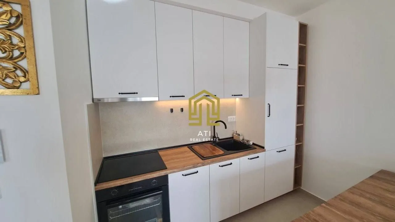 Moderna kuhinja sa bijelim elementima i drvenom radnom površinom.
