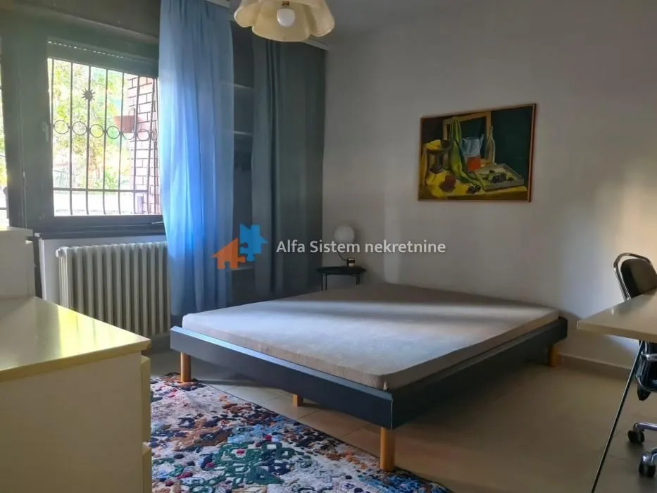 Furnished bedroom with a double bed, window, and a painting on the wall.