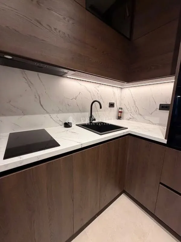 Modern kitchen with dark wood cabinetry, marble-style countertops, and a built-in cooktop.