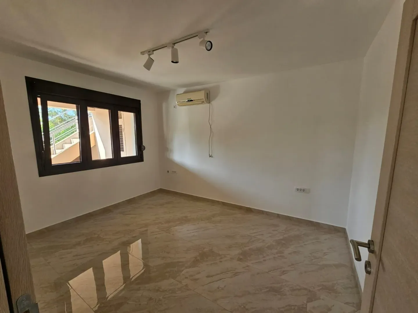 An empty, bright room with tiled floors and an air conditioning unit.