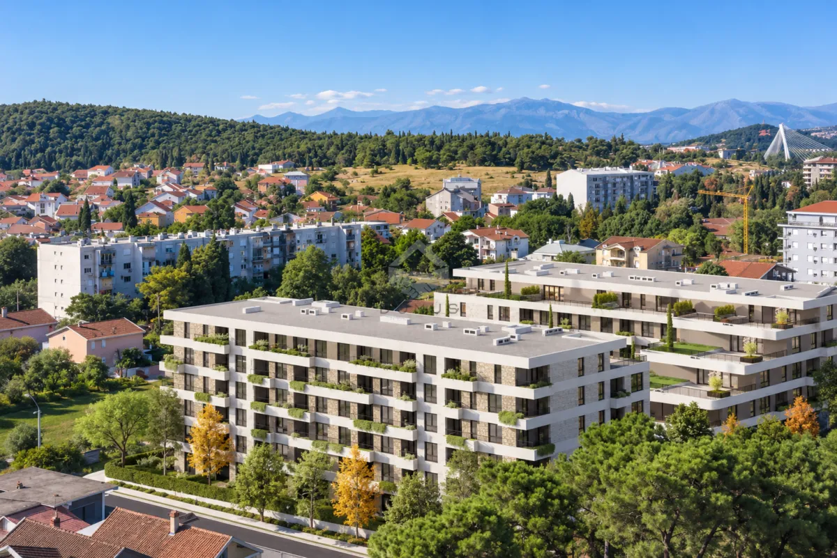 Pogled iz ptičje perspektive na novogradnju sa okolnim zelenilom i gradom u pozadini.