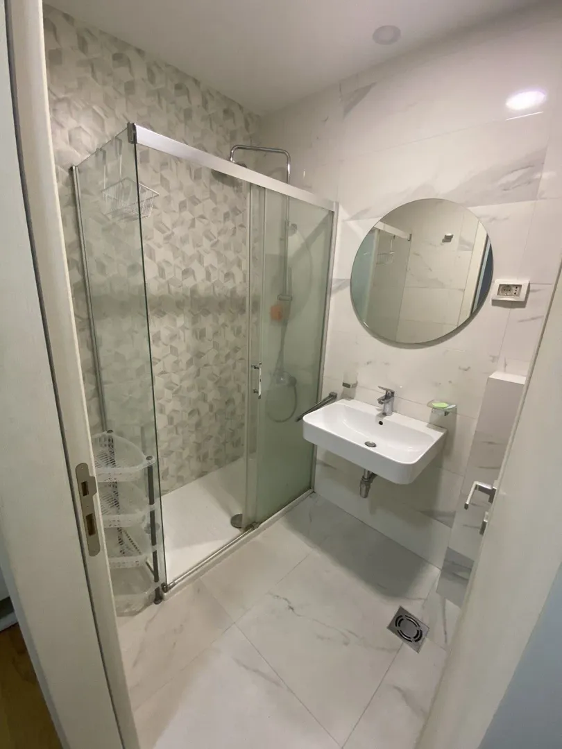 Modern bathroom with a glass shower cabin and a round mirror.