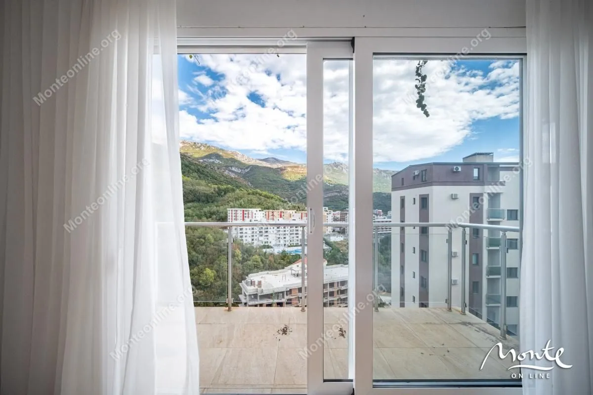View from the balcony overlooking surrounding buildings, hills, and blue sky.