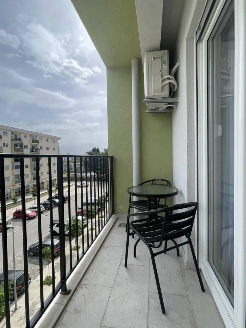 Small furnished balcony with a table, chairs, and a view of the street and parking.