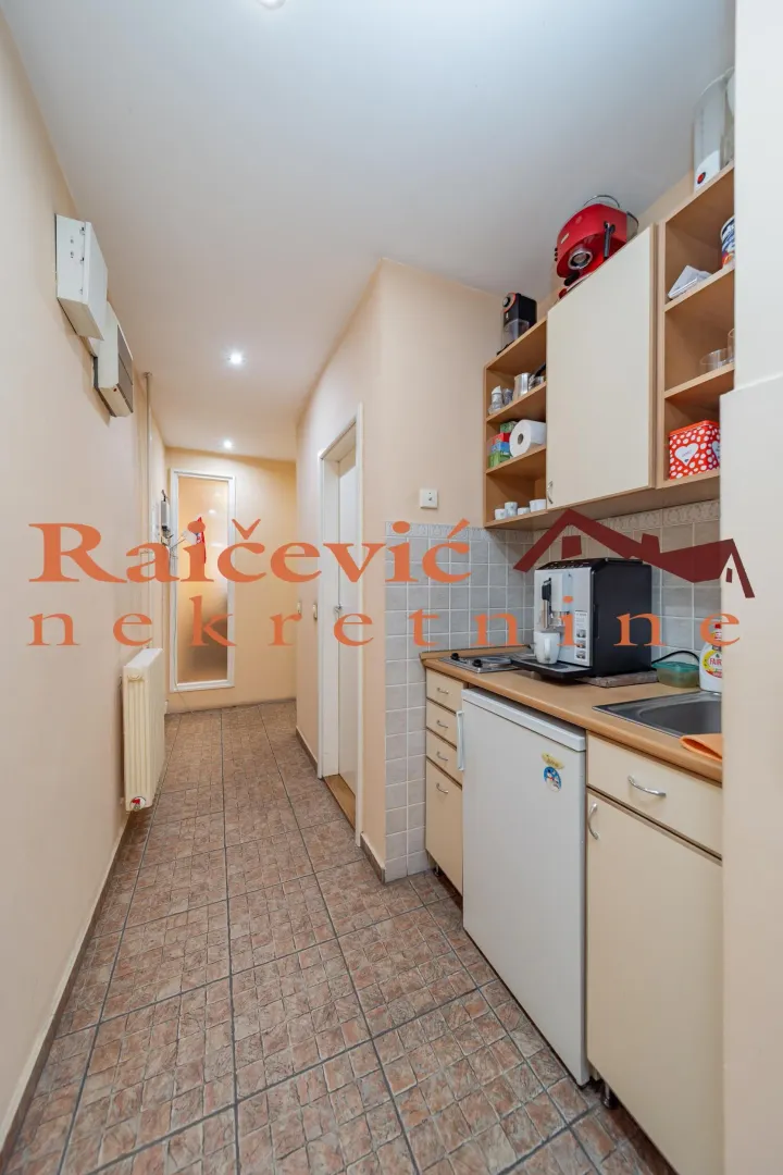 Small kitchenette in a hallway with cabinetry and appliances.