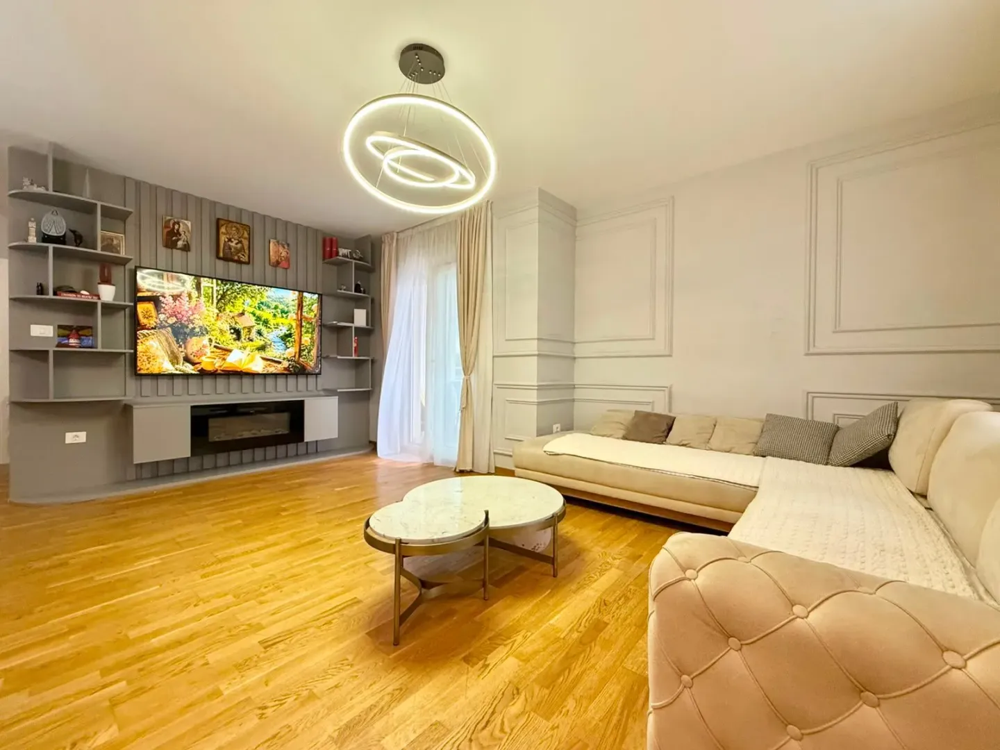 Prostrana i svijetla dnevna soba sa garniturom, TV-om i modernim lusterom.