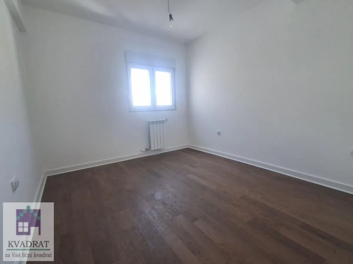 Empty room with white walls, dark parquet flooring and a single window.
