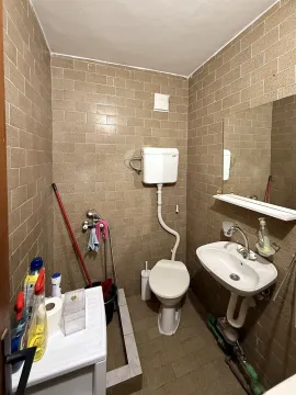 Manje kupatilo obloženo smeđim pločicama sa toaletom, umivaonikom i ogledalom. - image 8