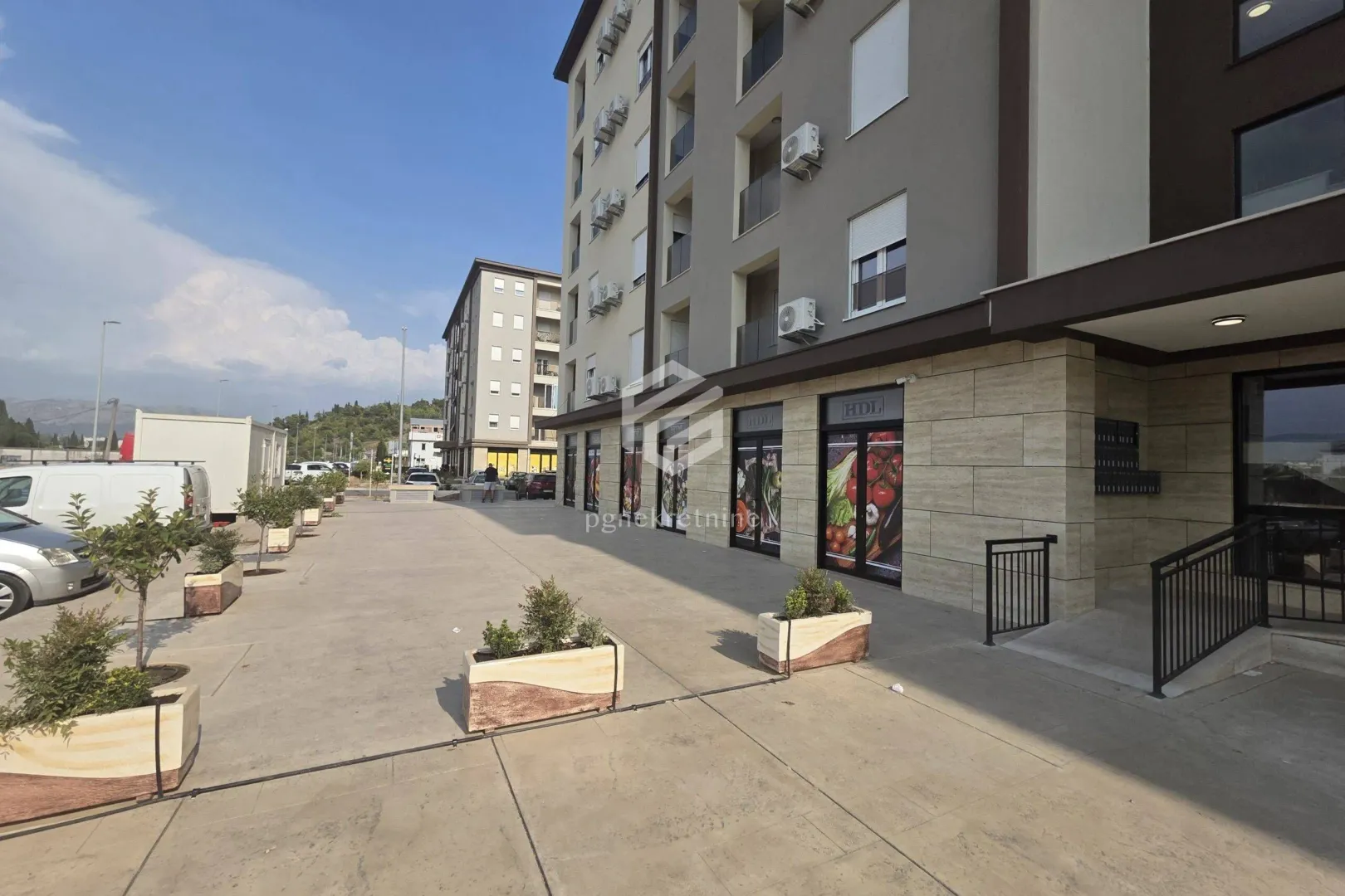 Eksterijer stambeno-poslovne zgrade sa popločanim dvorištem i žardinjerama.