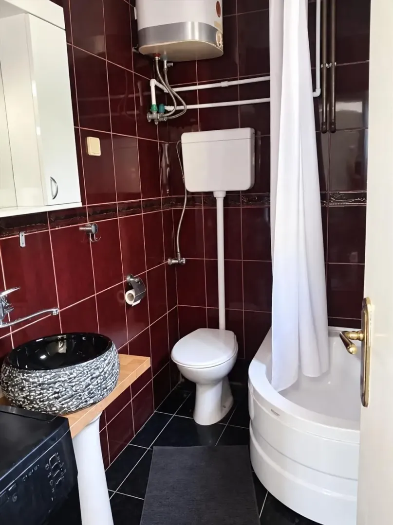 Bathroom with dark red tiles, bathtub, toilet, and washbasin.
