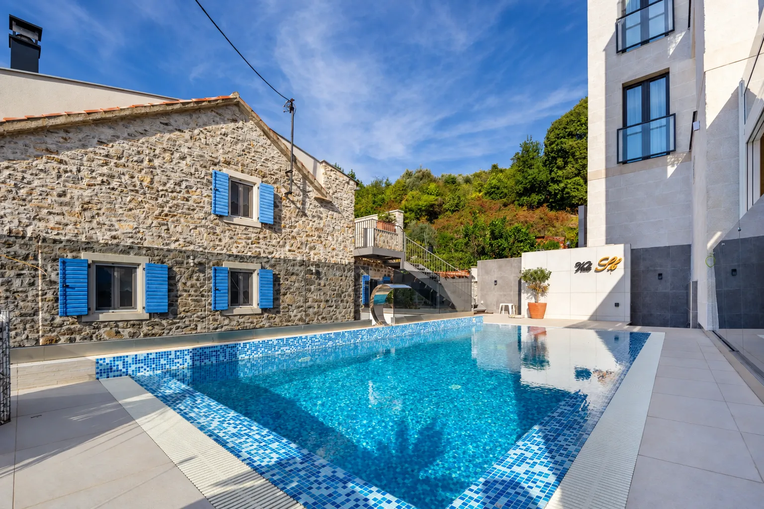 Swimming pool in front of a traditional stone house and modern building.