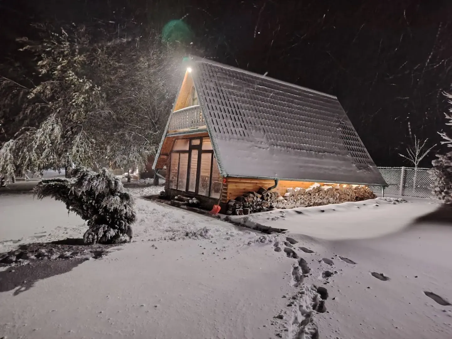 Pogled na drvenu vikendicu noću pod snegom.