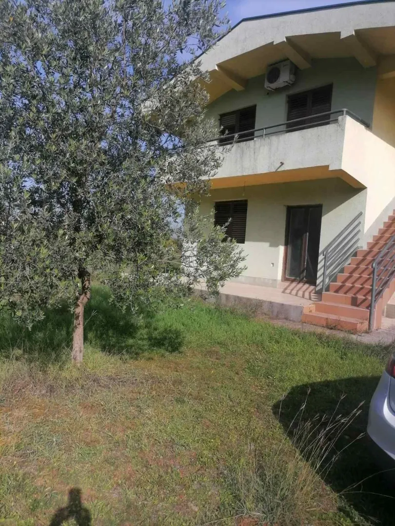 Dvospratna kuća sa dvorištem i stablom masline u prvom planu.