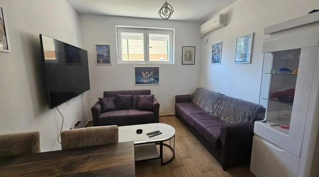 Dnevna soba sa garniturom, televizorom i trpezarijskim stolom.