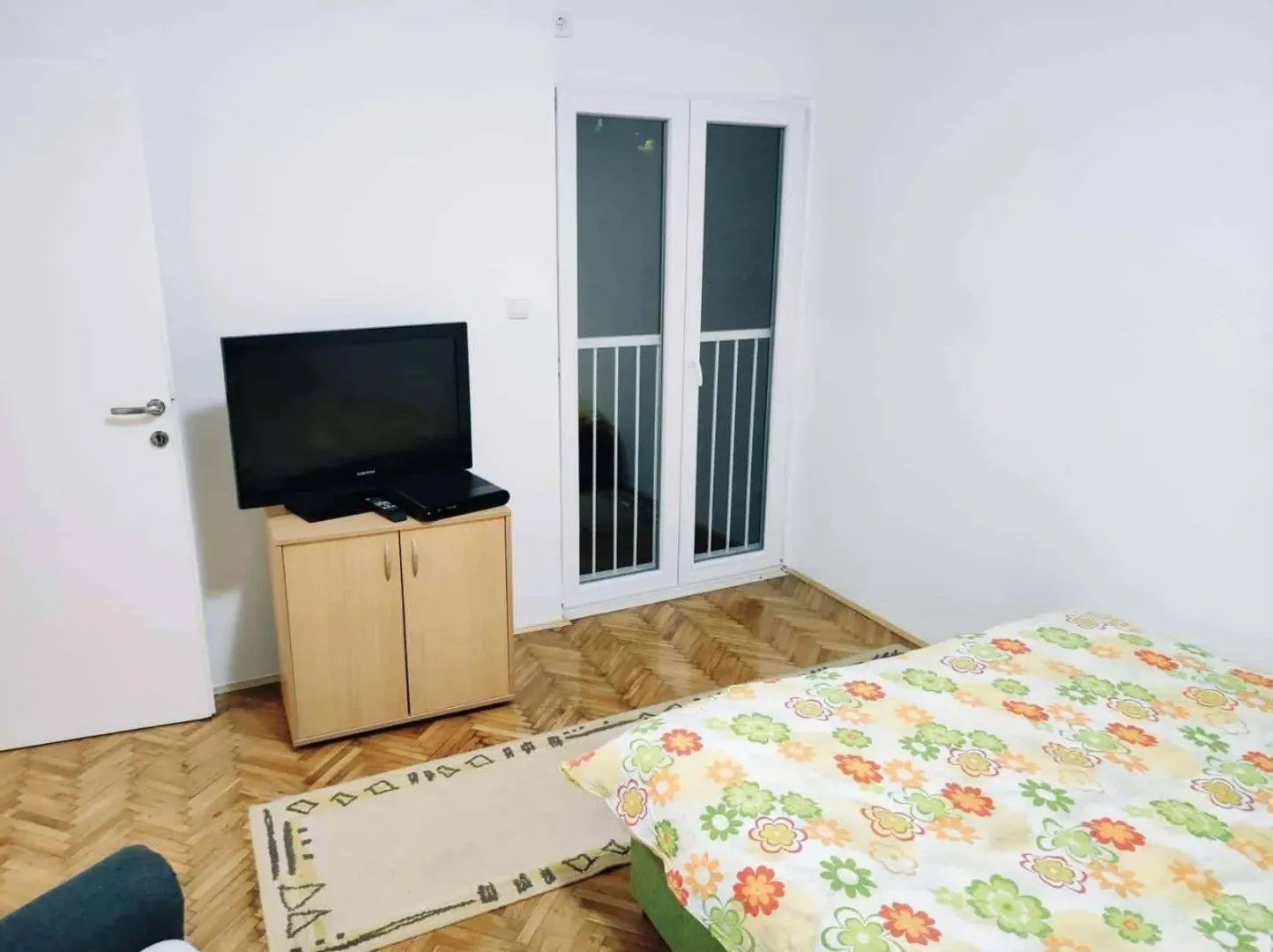 Namještena spavaća soba sa krevetom, komodom i televizorom.