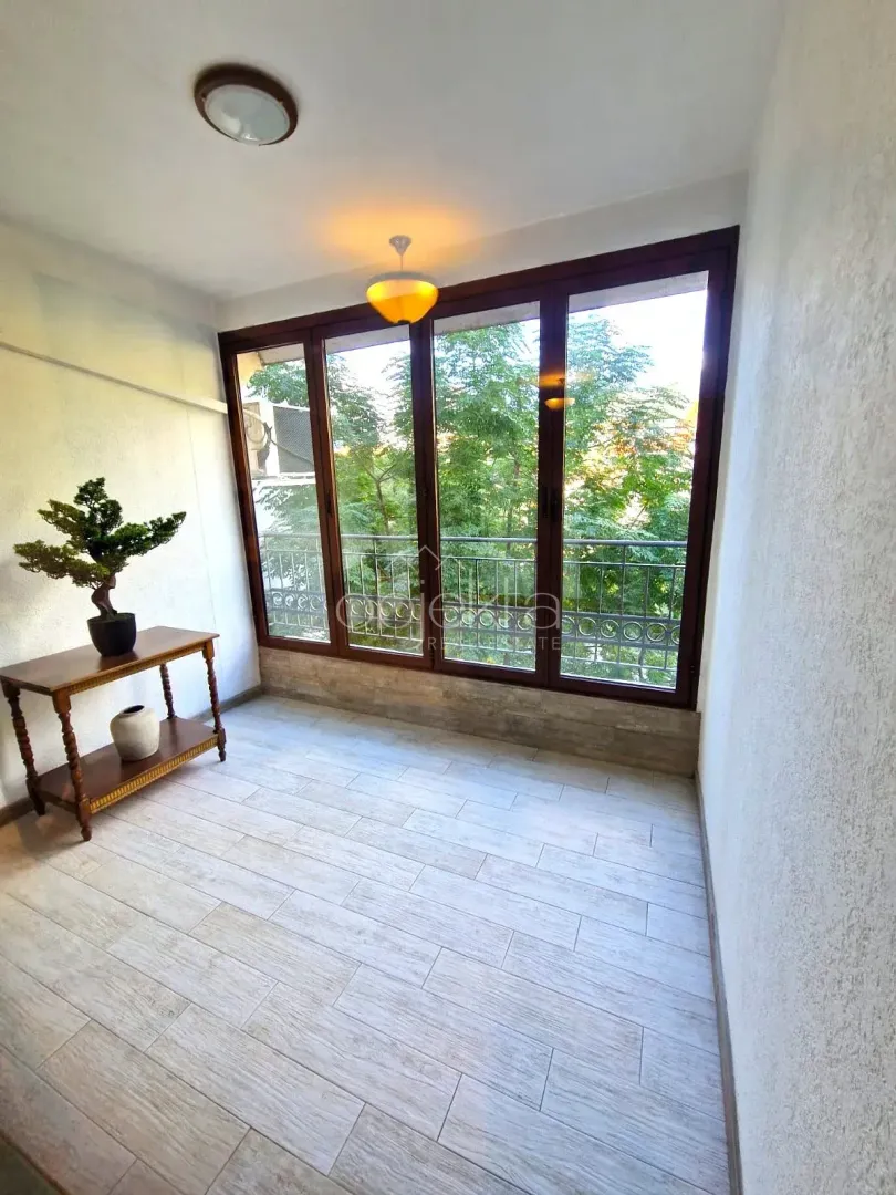Enclosed balcony with a wooden console table and a view of greenery.