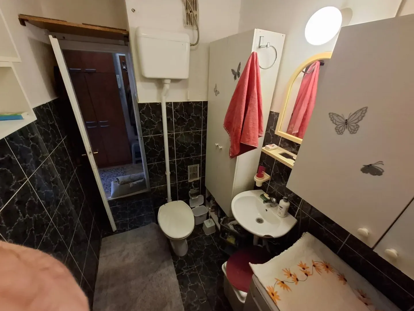 Manje kupatilo sa umivaonikom, WC šoljom i tamnim pločicama.