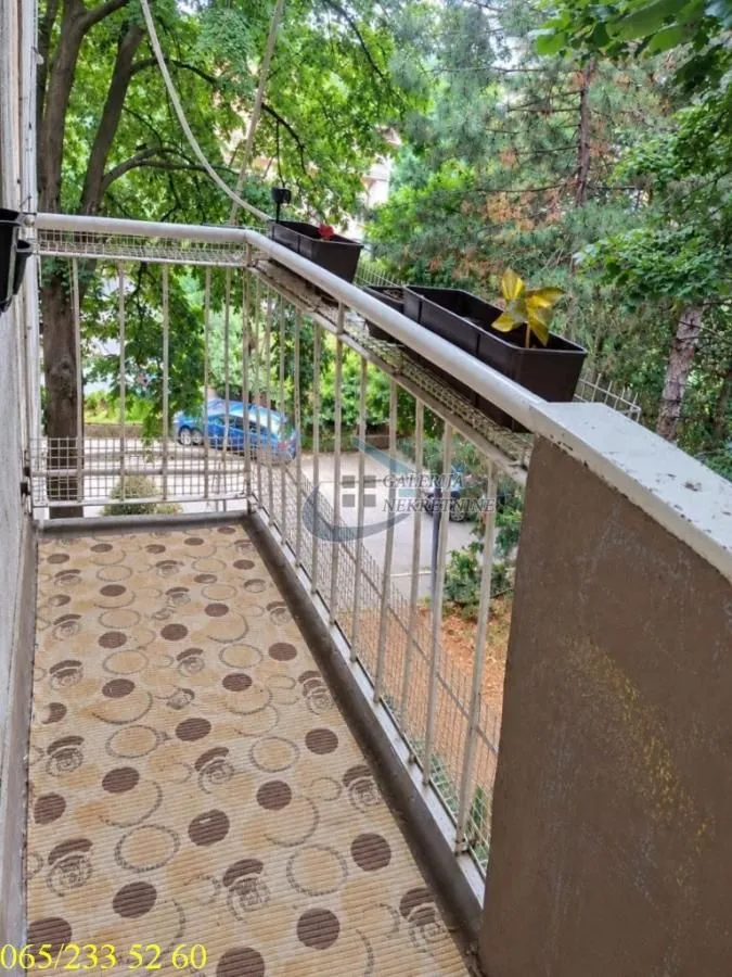 Manji balkon sa metalnom ogradom i pogledom na zelenilo i ulicu.