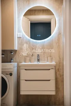 Bathroom with a vanity sink, cabinet, large round backlit mirror, and washing machine. - image 17