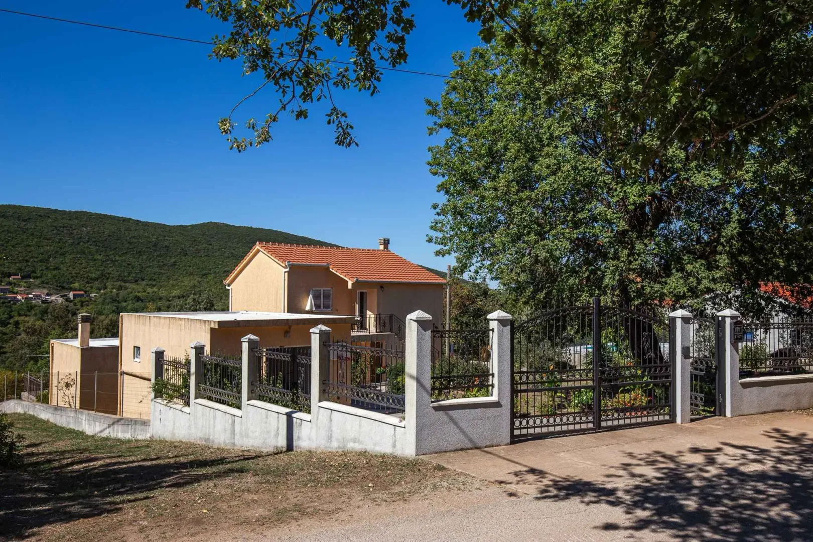 Pogled na spoljašnjost kuće sa dvorištem i ogradom.