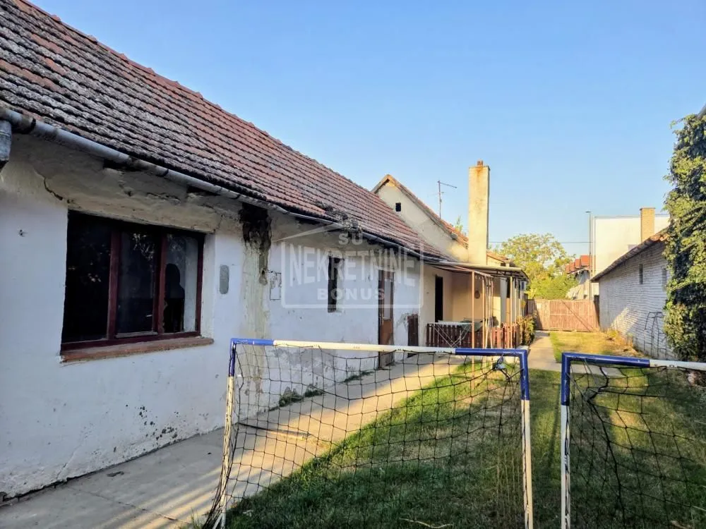 Pogled na dvorište i stariju kuću sa pomoćnim objektom i golovima.