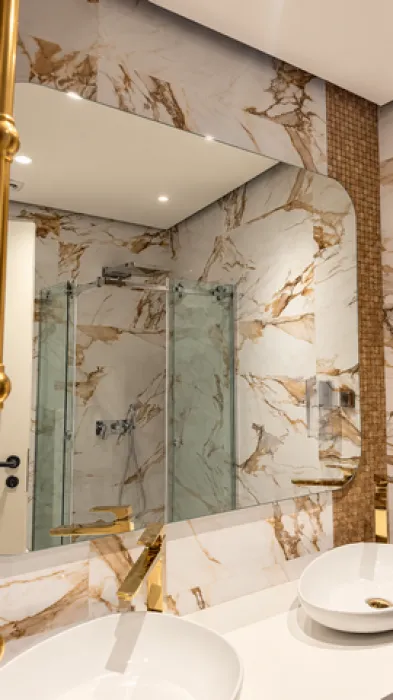 Modern bathroom with white washbasins, gold faucets, and a large mirror.