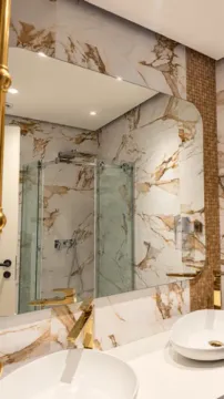 Modern bathroom with white washbasins, gold faucets, and a large mirror. - image 5