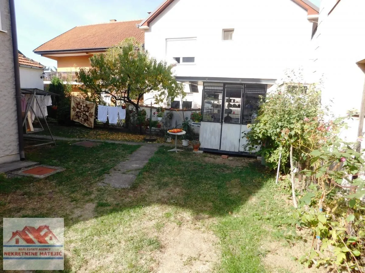 Dvorište kuće sa travnjakom, drvećem i pomoćnim objektom.